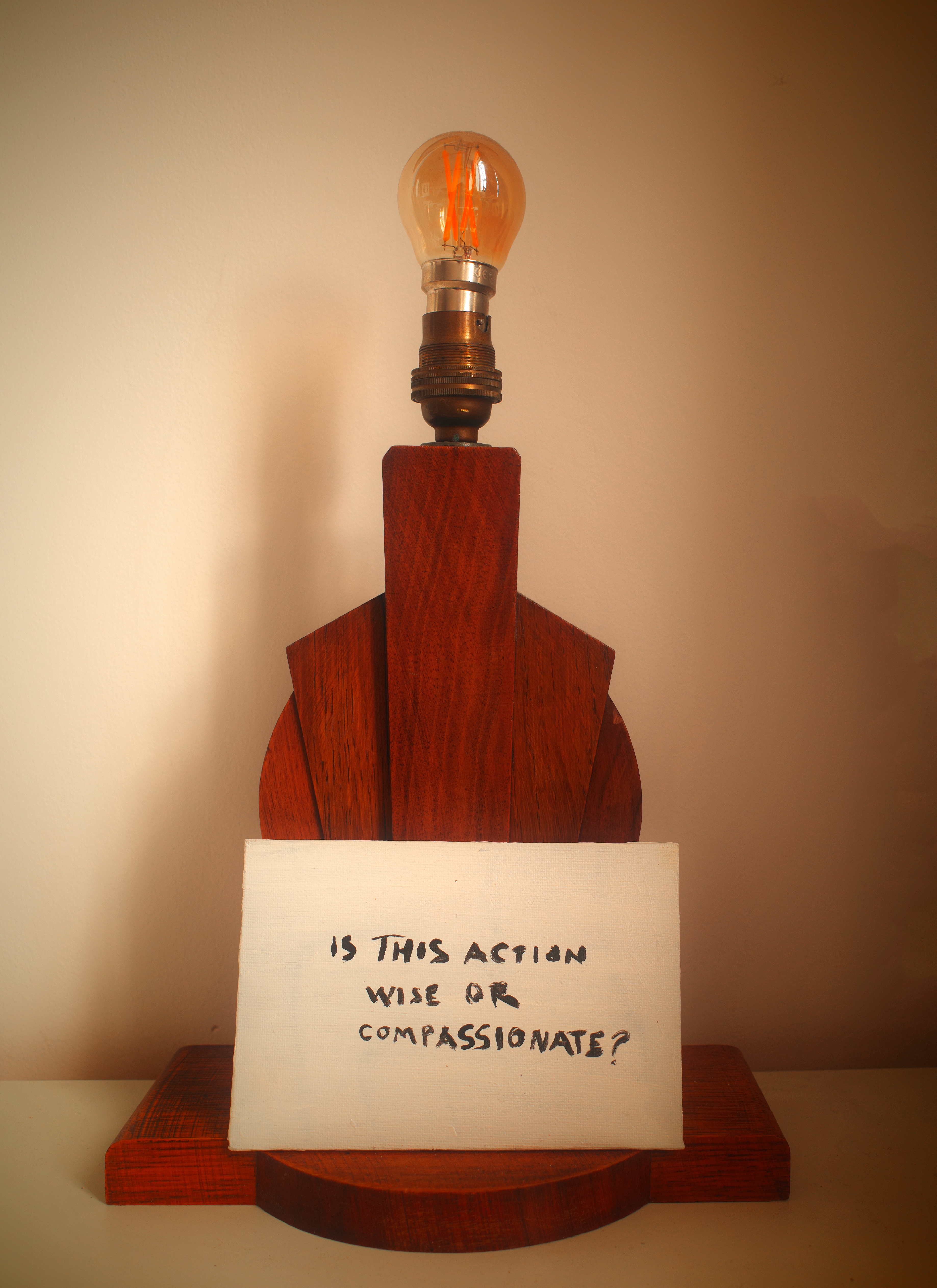 A wooden lamp beside a hand painted sign asking whether an action is wise or compassionate.